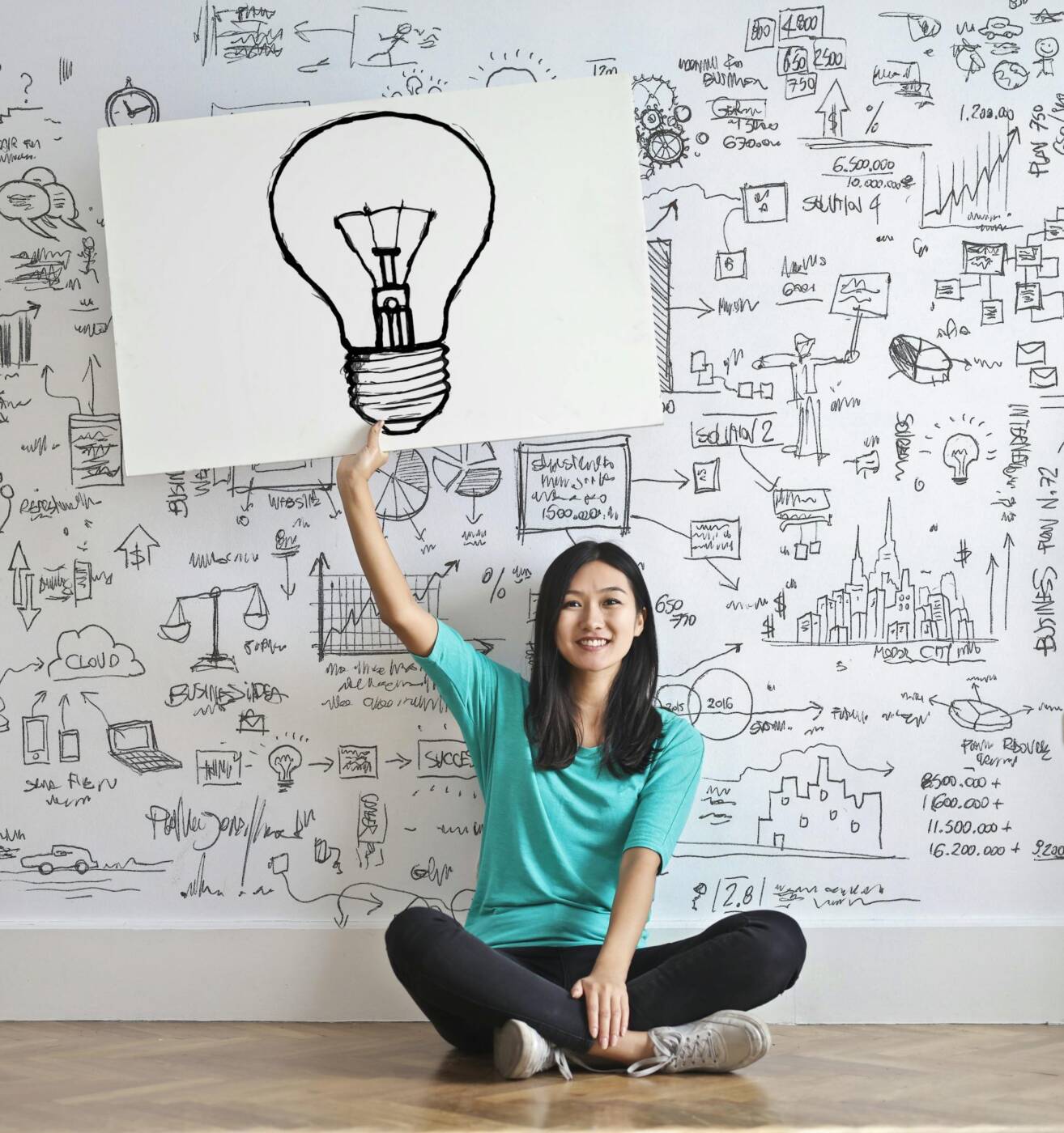 Woman holding a sheet of paper with a light bulb drawn in front of a whiteboard